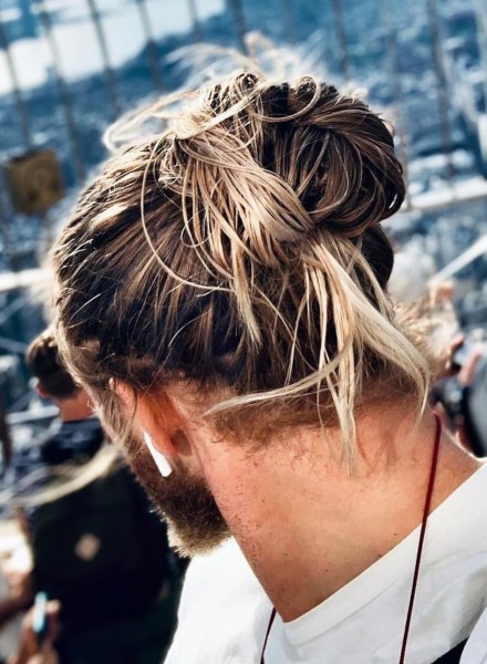 A male bun hairstyle with bright highlights.